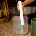 Load image into Gallery viewer, Hand holding a white cylindrical sonic mallet over a crystal sound bowl on a textured surface.