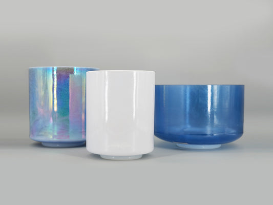 Three crystal sound bowls with iridescent, white, and blue finishes on a gray background