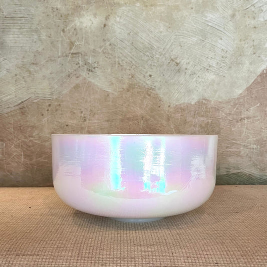 Iridescent crystal sound bowl on a textured surface with a neutral background