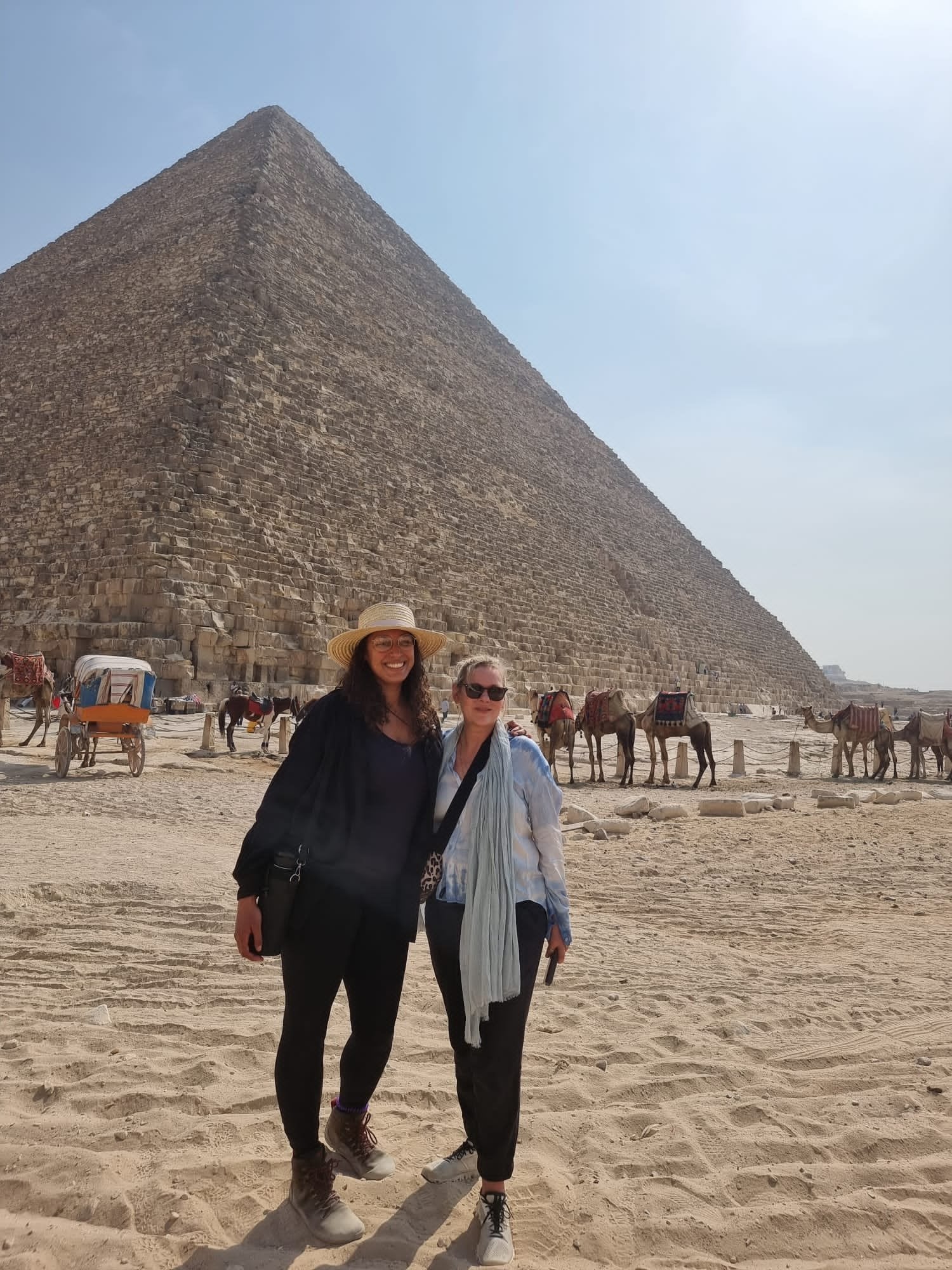 Kate and Casey standing in front of a pyramid with camels and carriages in the background.