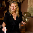 Load image into Gallery viewer, Woman - Kate - playing a set of singing bowls and holding a golden green practitioner crystal bowl by the stem. 
