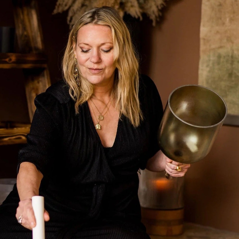 Woman - Kate - playing a set of singing bowls and holding a golden green practitioner crystal bowl by the stem. 