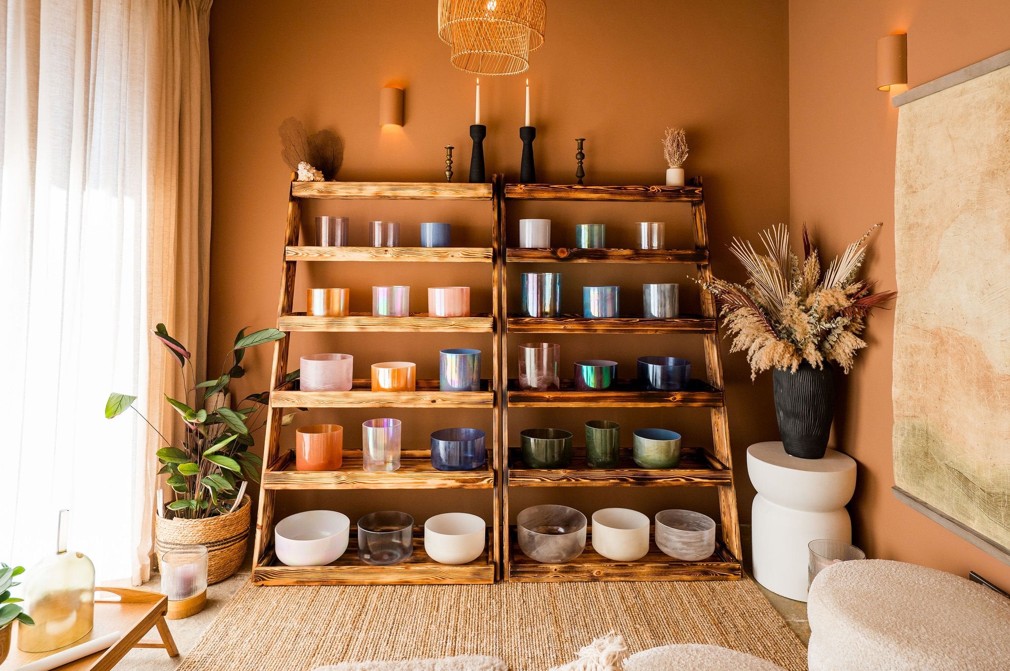 Wooden shelf with various crystal sound bowls in a cosy room with plants 