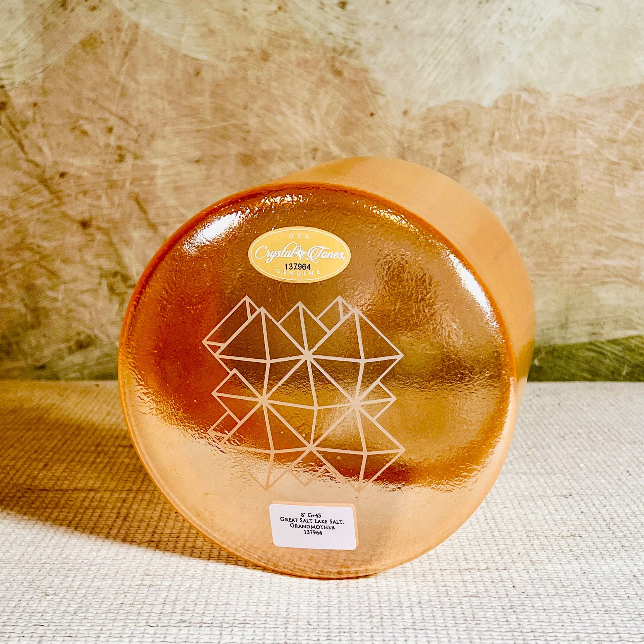 Round orange crystal sound bowl with geometric design on a textured surface