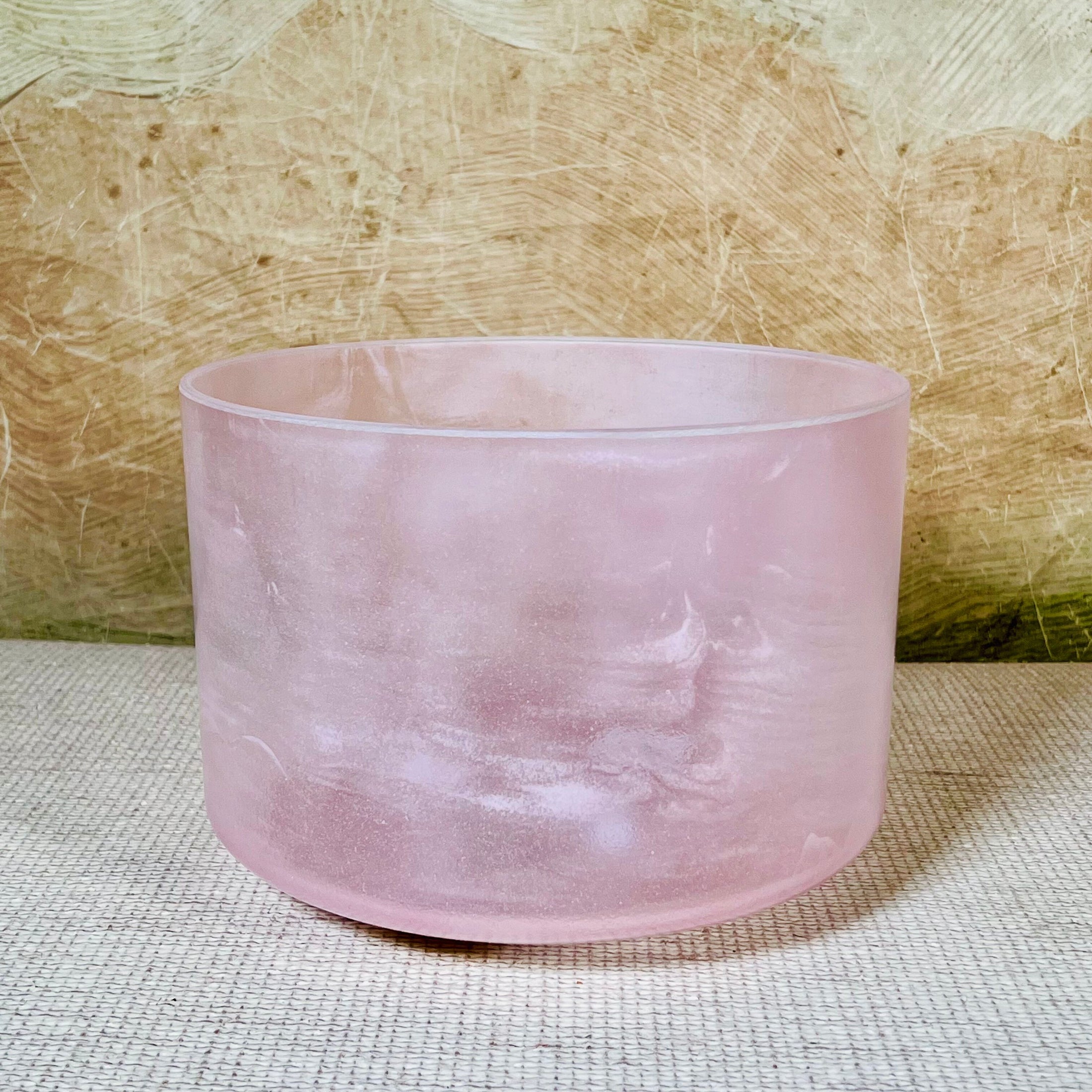 Pink crystal sound bowl on a textured surface with a neutral background