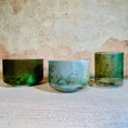 Load image into Gallery viewer, Three green crystal sound bowls of different sizes on a textured surface with a stone wall background.
