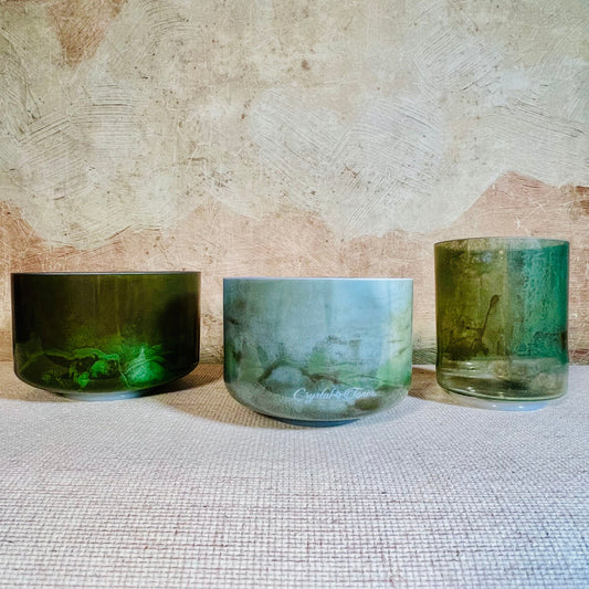 Three green crystal sound bowls of different sizes on a textured surface with a stone wall background.