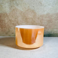Load image into Gallery viewer, Cylindrical crystal sound bowl with orange glaze on a textured surface
