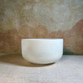 Load image into Gallery viewer, White crystal sound bowl on a textured surface with a beige background
