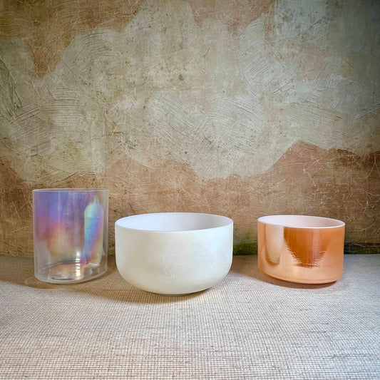 Three crystal sound bowls with different finishes on a textured surface.