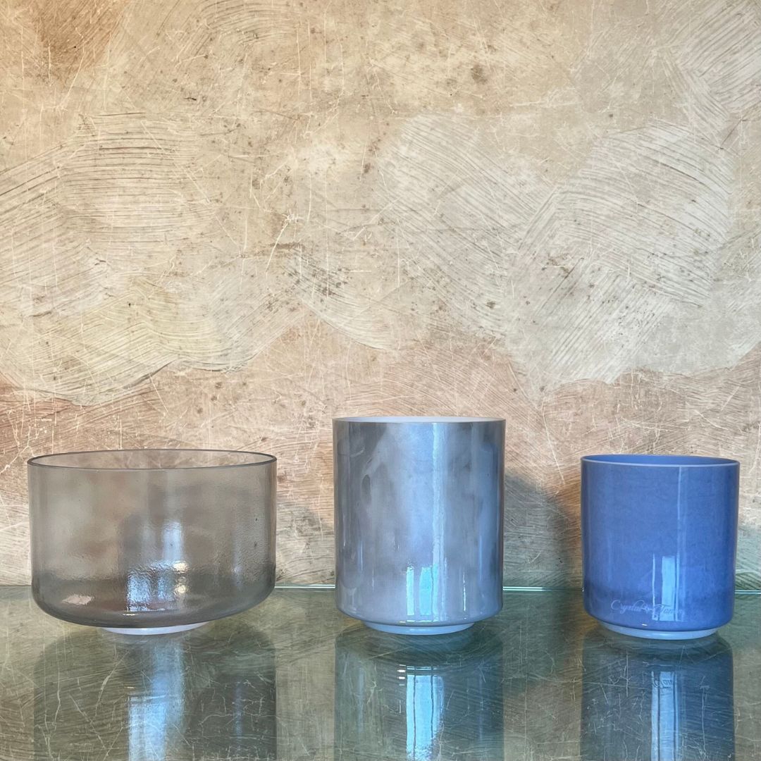 Starwater full set of three quartz crystal singing bowls in diamond, light blue grey iridescent, and egyptian blue on a reflective surface with a textured beige wall background.